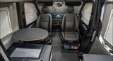 Inside an RV rental: black leather front seats, a circular table with bench seating, and window privacy blinds.