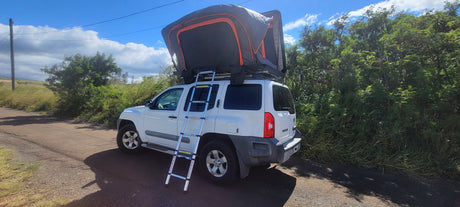 White Nissan Xterra SUV with a deployed rooftop tent and ladder, ideal for your rv rental adventure.