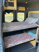 Cozy RV rental camper van interior with practical bunk beds and a control panel, perfect for road trips and camping.
