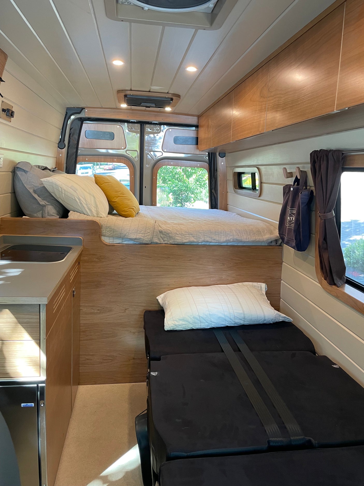 Cozy RV rental interior: elevated bed, convertible lower bed/seating, compact kitchenette, and wood accents.