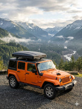 Orange Jeep Wrangler with a rooftop cargo box against a stunning mountain and river vista. Ideal for an RV rental adventure.