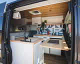 Explore this modern **rv rental** interior, featuring a compact kitchen with a sink, cooktop, wood countertops, and a pull-out table.