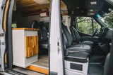 A peek inside a sleek rv rental camper van: comfortable front cabin seats and a stylish custom-built living area with wood accents.