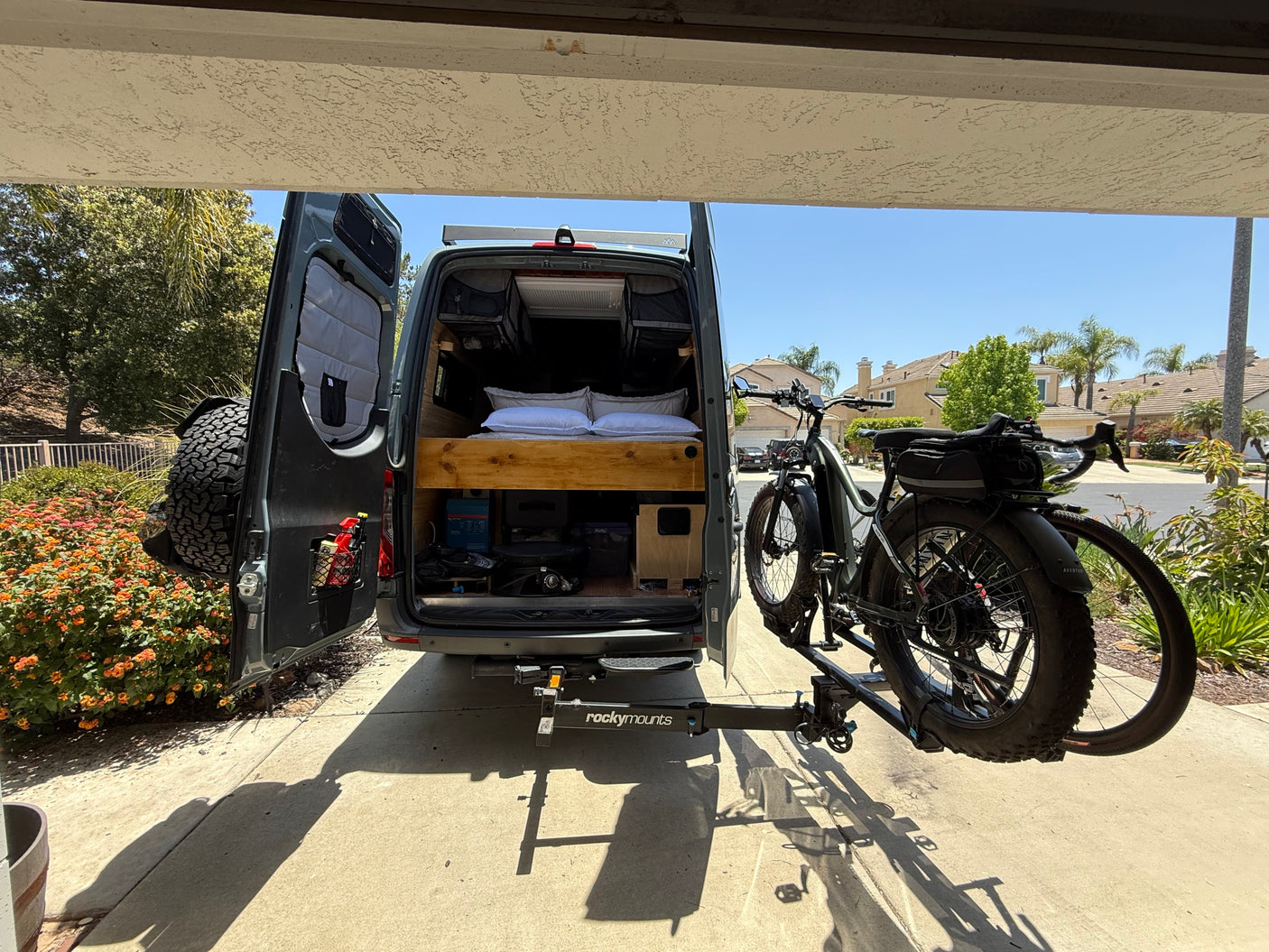 This RV rental camper van displays its custom interior with a bed & an e-bike on a RockyMounts rack, ready for adventure.