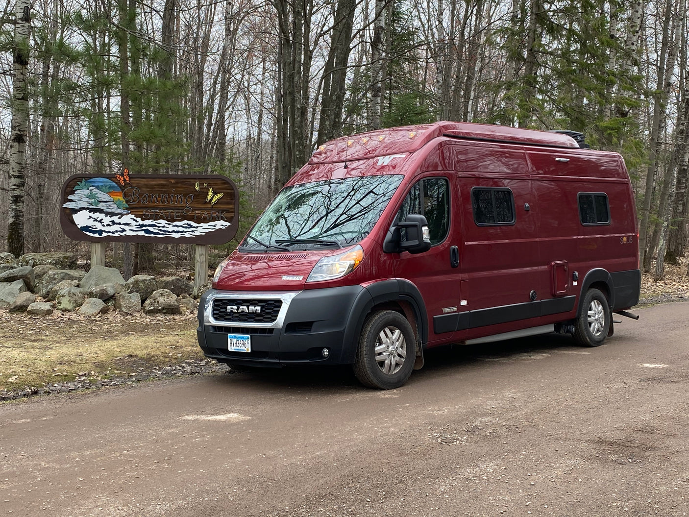 Red campervan rental at Banning State Park, MN, parked on a dirt road in a wooded setting.