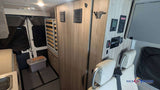 This RV rental camper van interior features a control panel, bed frame, rear screened doors, and floor storage.