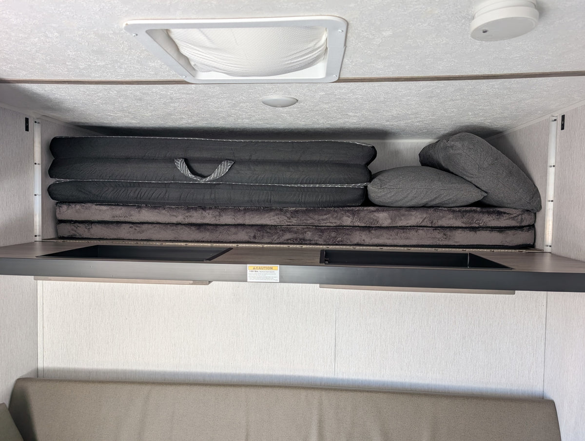 RV rental overhead bunk area with stacked mattresses, pillows, ceiling vent, and a 150 lbs. weight limit. — photo 15