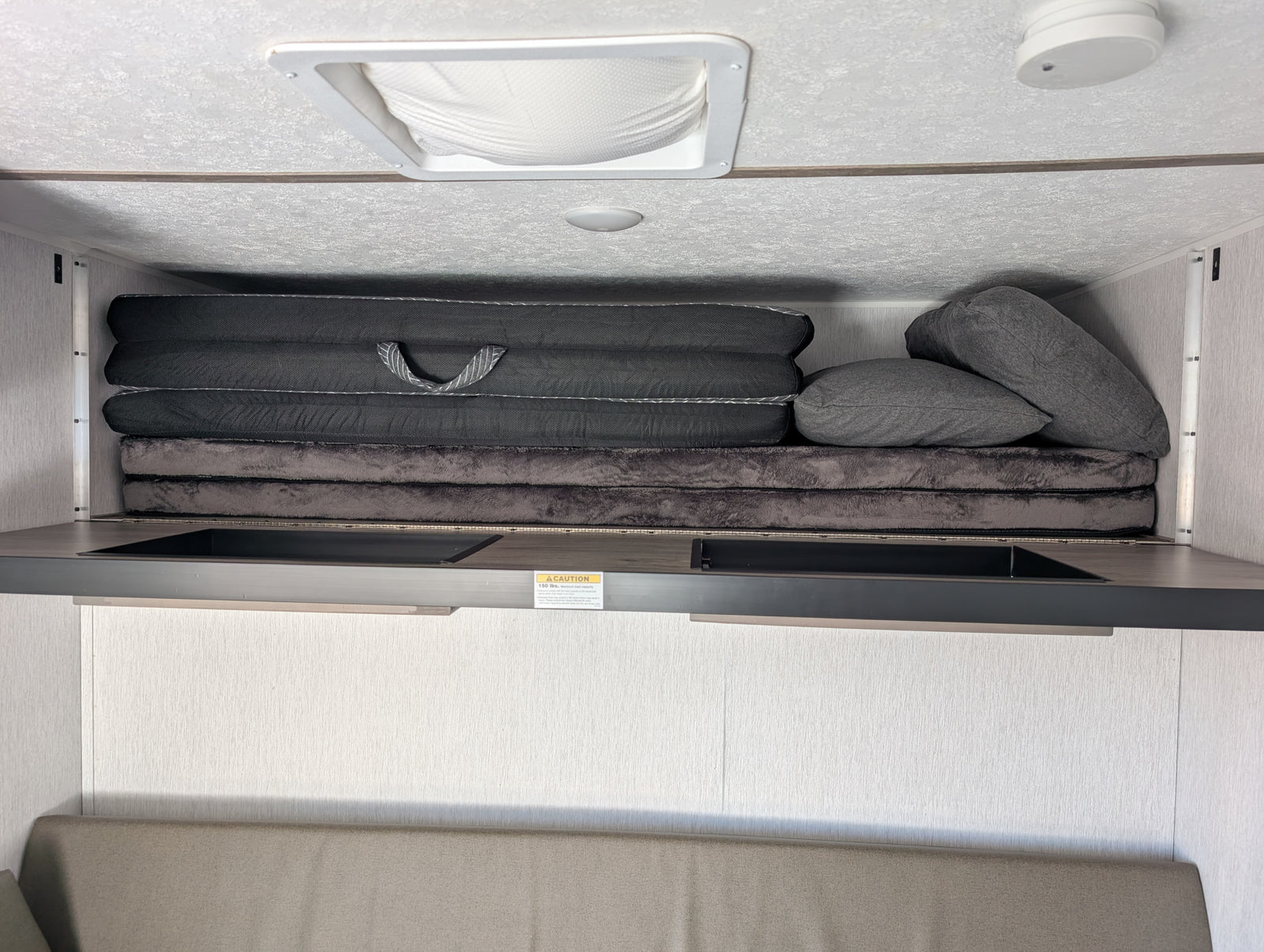 RV rental overhead bunk area with stacked mattresses, pillows, ceiling vent, and a 150 lbs. weight limit.