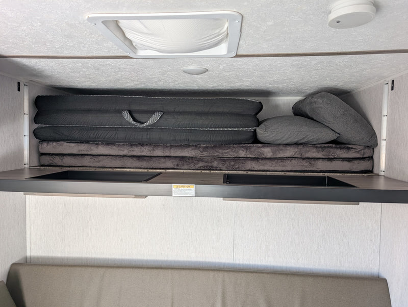 RV rental overhead bunk area with stacked mattresses, pillows, ceiling vent, and a 150 lbs. weight limit. — photo 15