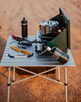 RV rental camp kitchen: Portable table with a green camping stove, pot, pan, cutting board, and diverse tools for outdoor cooking.