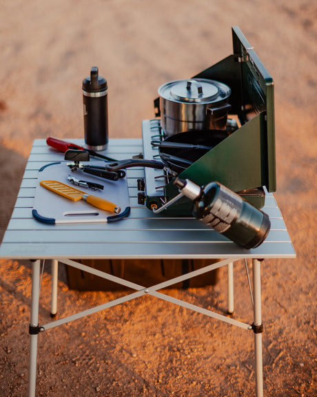 RV rental camp kitchen: Portable table with a green camping stove, pot, pan, cutting board, and diverse tools for outdoor cooking.