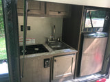 Compact RV rental kitchen features Dometic stovetop, sink, microwave, and refrigerator, ideal for travel.