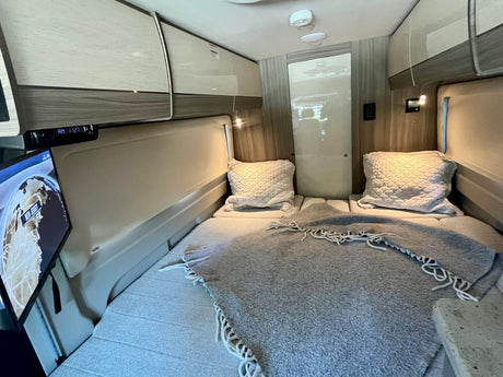 Inside this RV rental, find a modern bedroom with comfortable twin beds, overhead storage, and a TV for restful journeys.