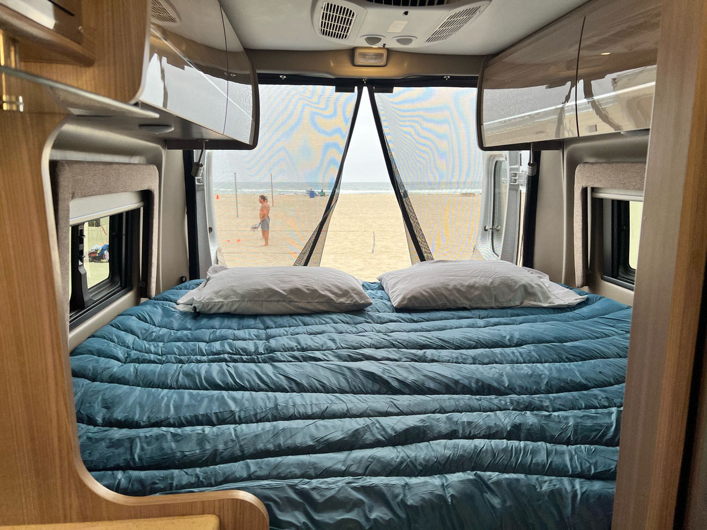 Inside a comfy RV rental, featuring a bed with a direct beach and ocean view through the open rear. — photo 9