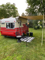 This cozy vintage RV rental features an awning, outdoor chairs, and a lit tiki torch, perfect for a relaxing campsite evening.