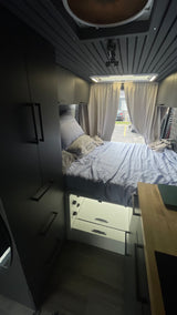 Cozy RV rental interior: elevated bed with storage, dark cabinetry, and rear window view.