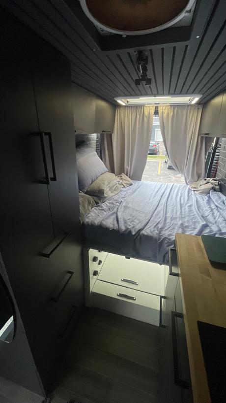 Cozy RV rental interior: elevated bed with storage, dark cabinetry, and rear window view.