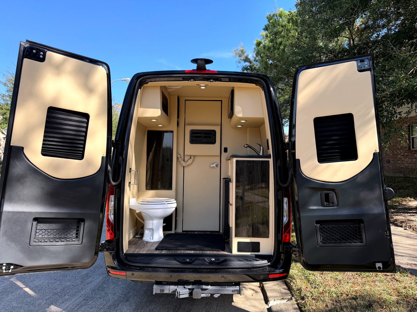This rv rental's open rear doors reveal a functional interior: toilet, sink, and tan cabinets under bright lights. — photo 2