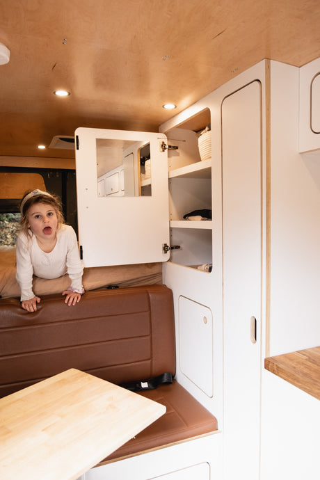 A playful child pops up in a custom RV rental, showcasing its cozy interior, storage, and comfortable seating.