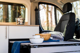 RV rental: Interior of a cozy camper van, showcasing a functional kitchenette and dining area with nature visible outside.