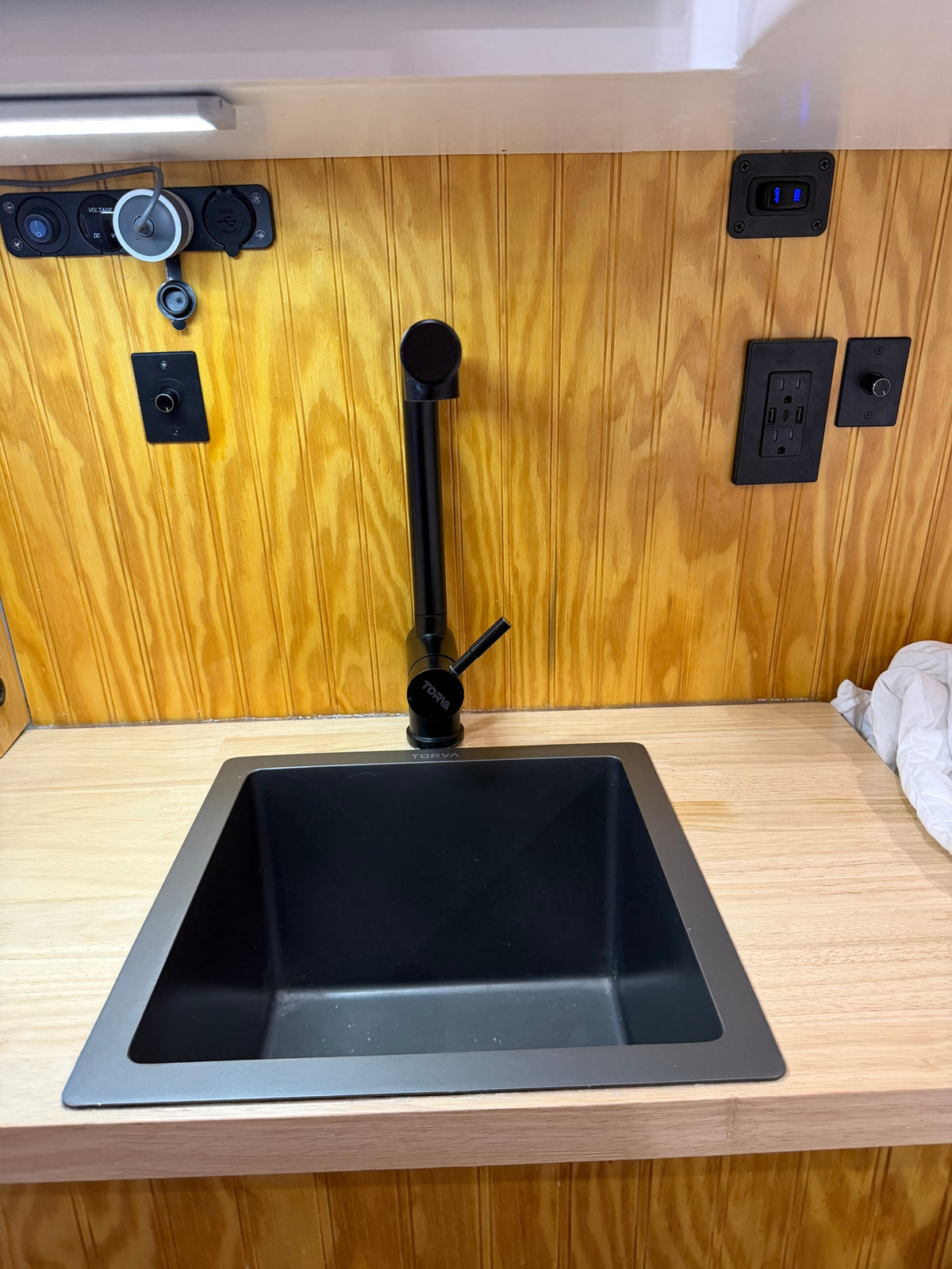 RV rental interior: black sink, Torva faucet, wooden counter & wall paneling, with integrated power outlets & USB ports. — photo 7