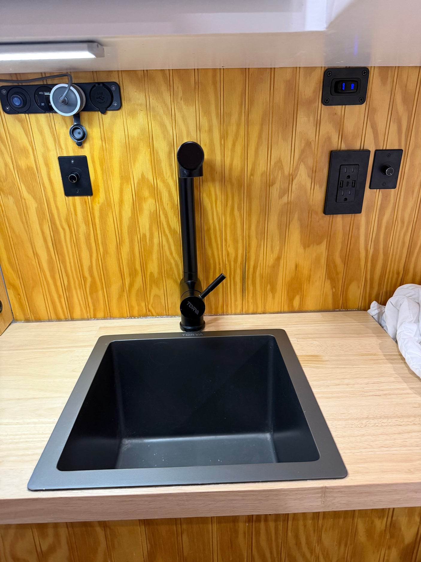 RV rental interior: black sink, Torva faucet, wooden counter & wall paneling, with integrated power outlets & USB ports.