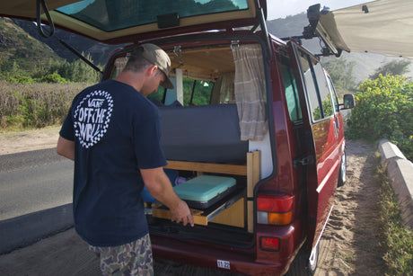 Man accessing portable kitchen from red RV rental. Perfect for van life adventures with stunning mountain views.