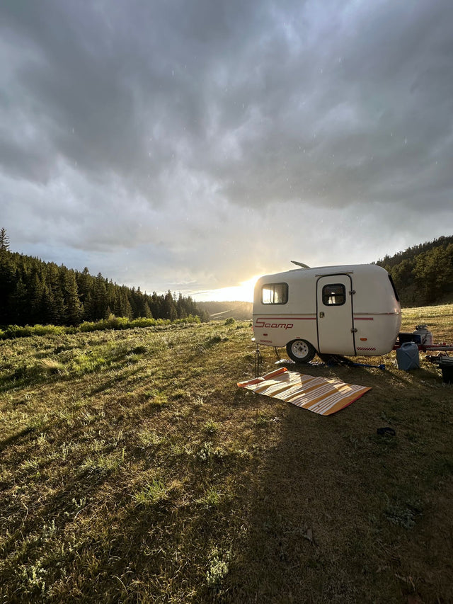  tree-lined campsite under a partly cloudy sky. Ideal for nature lovers.|Scenic camping with an RV rental. A white Scamp trailer under a sun-drenched