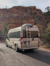 Tan RV rental van parked on a scenic road with majestic red rock mountains in the background.