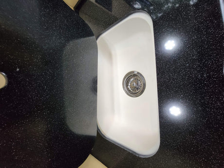 Functional RV rental kitchen area: white sink, black speckled countertop, and overhead light reflections.