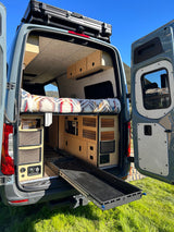 Explore van life! This custom camper van interior, ideal for an RV rental, shows a cozy bed & convenient pull-out storage.