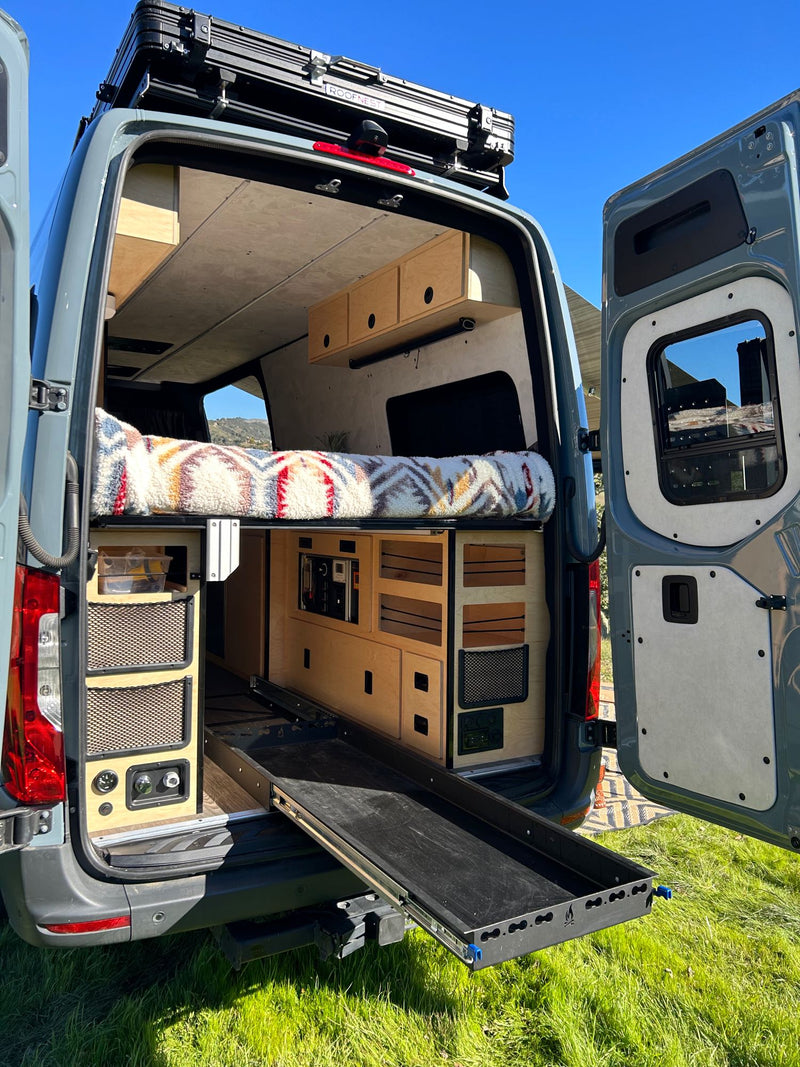 & mountain views from inside this camper van.|Cozy RV rental interior with a built-in projector screen over the comfortable bed and ample overhead storage.|Exploring nature with an **rv rental**! A custom van with surfboards is parked on a vibrant green hillside — photo 7