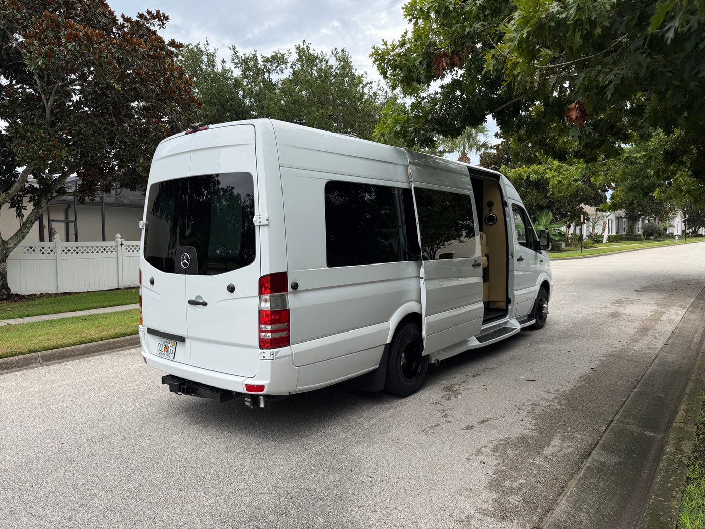 White Mercedes-Benz Sprinter rv rental van parked on a residential street with its side door open, revealing the customized interior. — photo 5