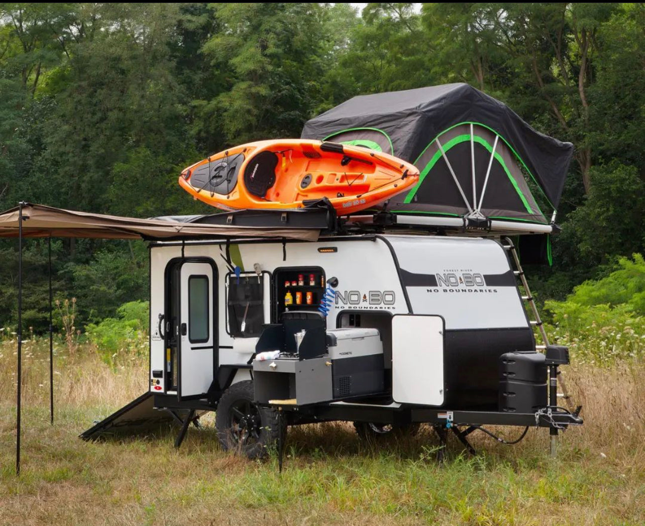 Small rv rental: a white camper trailer with an orange kayak, green tent, and outdoor kitchen. Perfect for adventure.