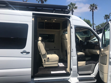 White luxury van, a premium RV rental, with its side door open revealing spacious, cream-colored interior seating.