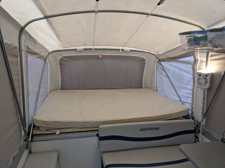 Inside a spacious RV rental, a pop-up camper with a large bed, seating, and overhead storage for camping comfort.