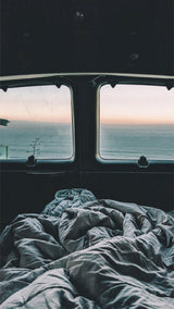 RV rental: A cozy bed offers serene ocean views from inside this camper van. Perfect for a peaceful getaway.