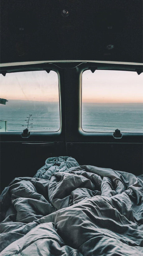 RV rental: A cozy bed offers serene ocean views from inside this camper van. Perfect for a peaceful getaway.