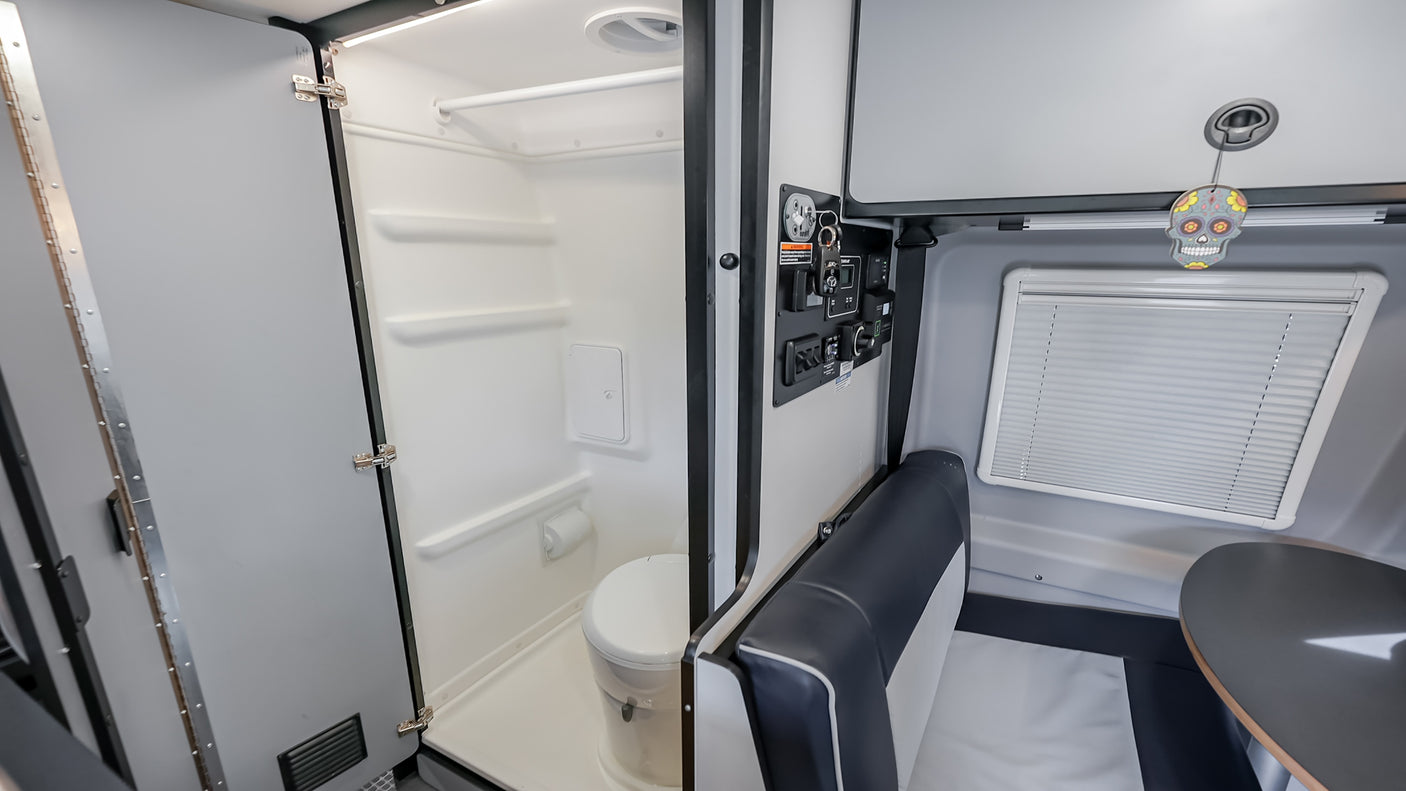 Explore this RV rental's interior: a compact bathroom with shower/toilet, control panel, and cozy dinette area.