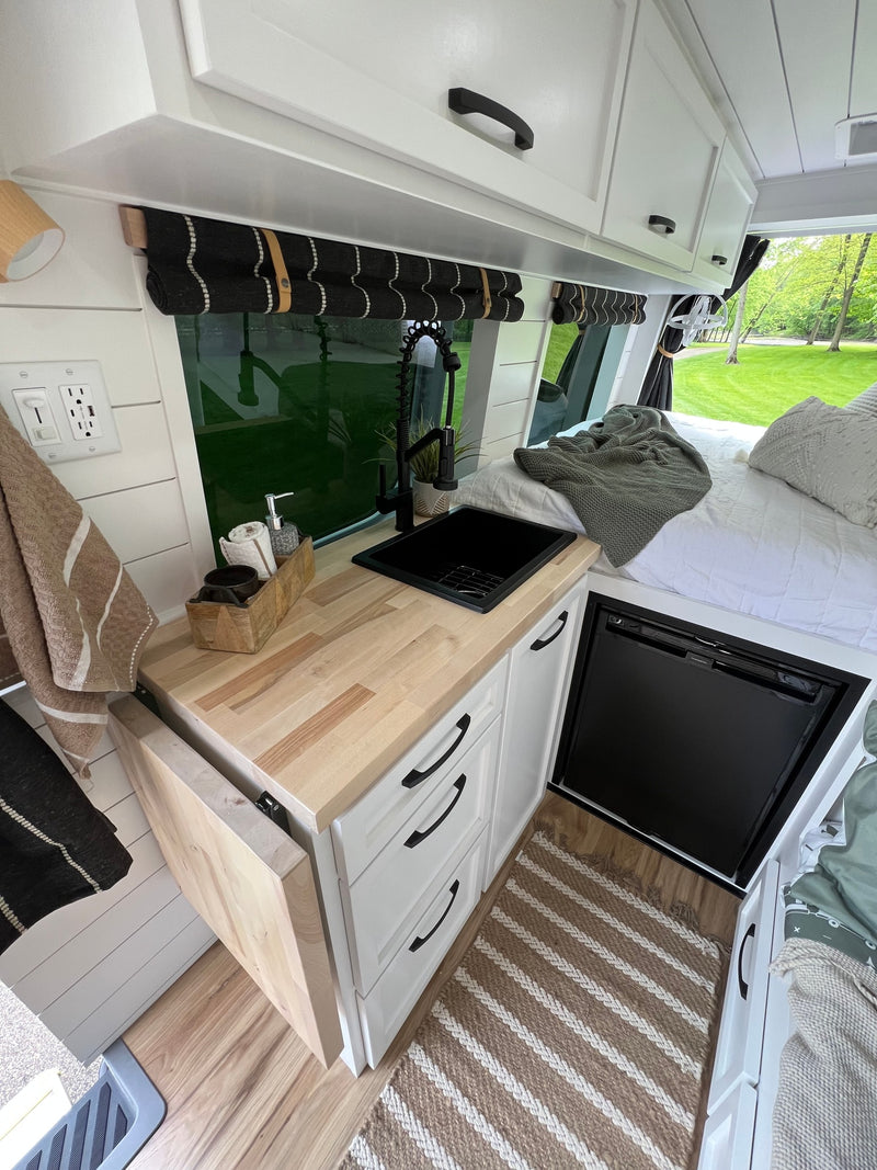 RV rental: Modern camper van interior shows a compact kitchen with wood counter, black sink/faucet, fridge, and bed. — photo 3