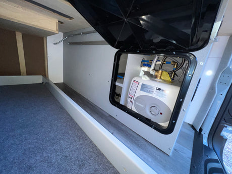RV rental: An open access panel reveals a Bosch water heater and its plumbing, integrated into the clean camper interior with storage.
