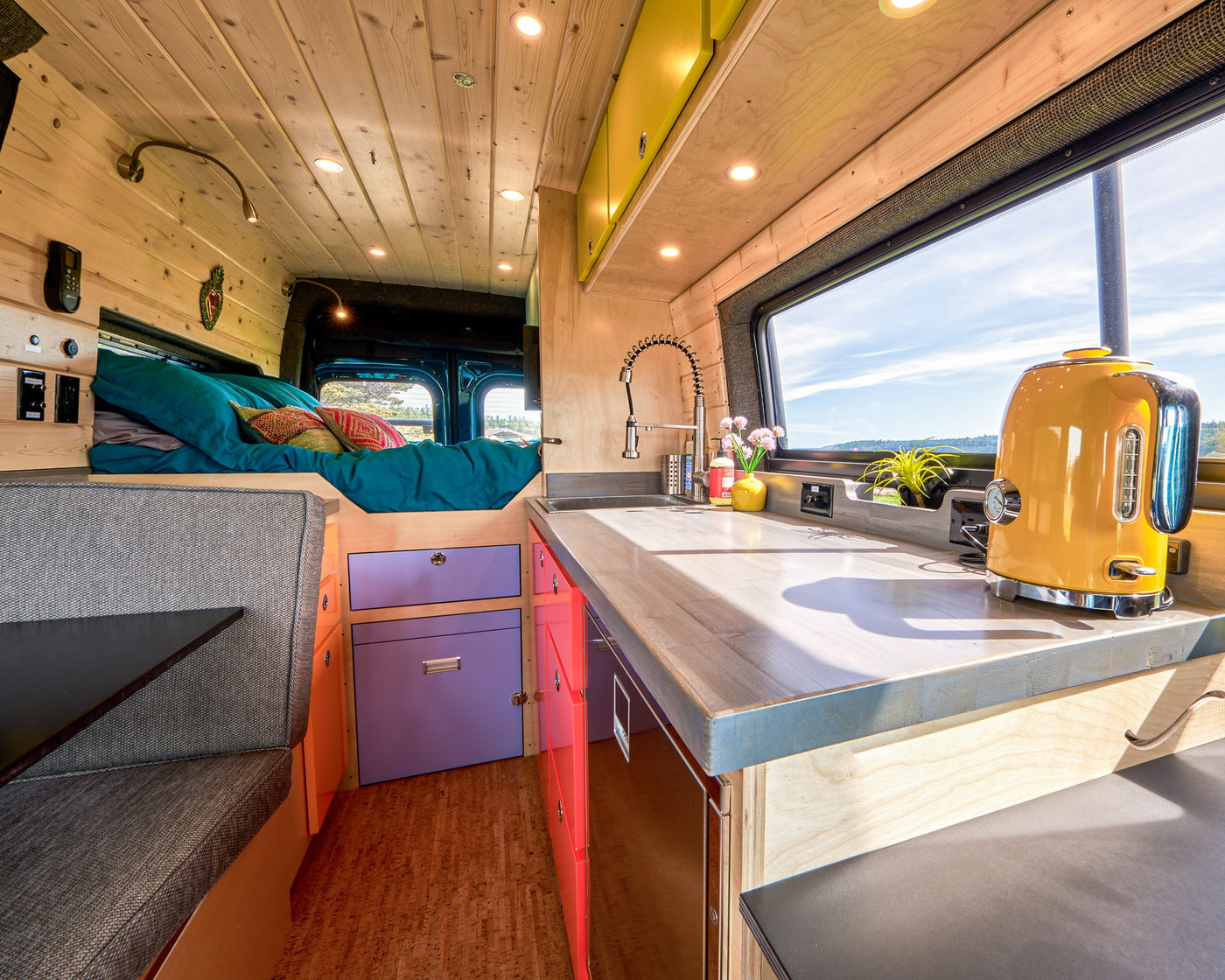 Vibrant RV rental camper van interior featuring a bright kitchen, cozy bed, and colorful custom cabinetry. — photo 6