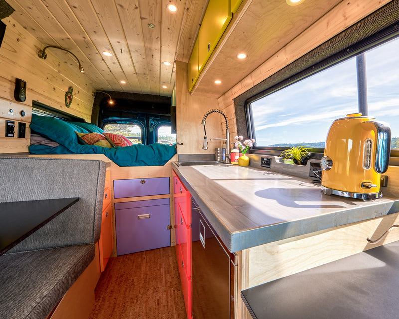 Vibrant RV rental camper van interior featuring a bright kitchen, cozy bed, and colorful custom cabinetry. — photo 6