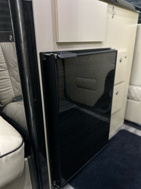 Inside this RV rental, you'll find a sleek black compact refrigerator, cream cabinets, and luxury quilted leather seating.
