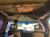 This RV rental's interior reveals the front seats, dashboard, overhead storage, and a small fan. A clear view out the windshield.