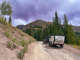 Off-road RV rental and Jeep exploring a mountain trail under a dramatic sky.