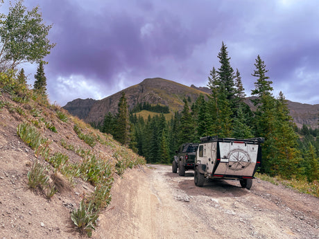 Off-road RV rental and Jeep exploring a mountain trail under a dramatic sky.