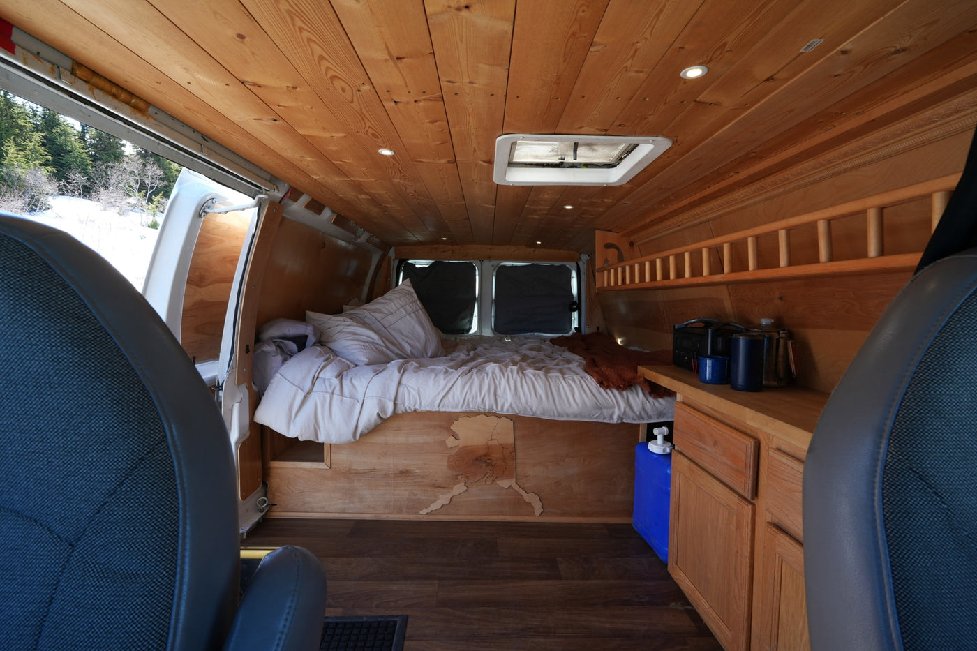 Experience a unique RV rental: a custom wood-paneled camper van interior with a bed, counter, and scenic snowy views. — photo 6