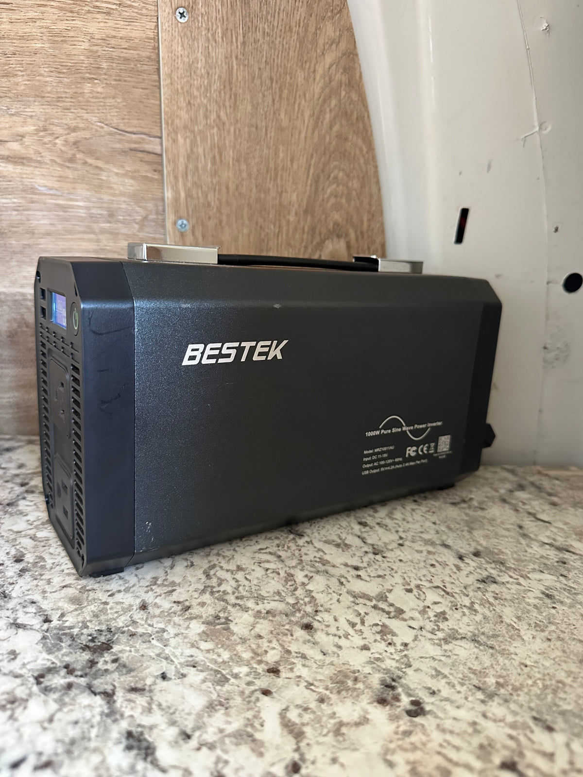 A black BESTEK 1000W pure sine wave power inverter for an rv rental, offering portable power. It sits on a speckled counter. — photo 20