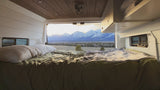 Relax in an RV rental bed with stunning views of snow-capped mountains at sunrise/sunset. Perfect for memorable adventures.